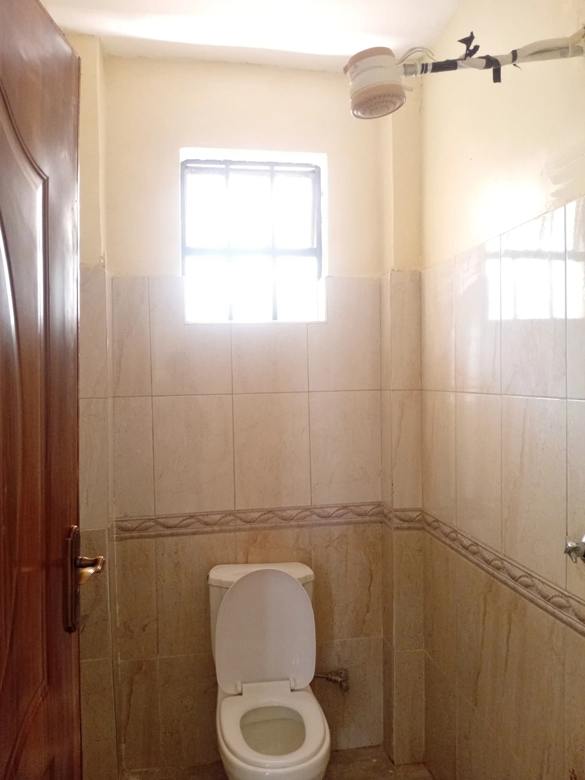 Compact bathroom with toilet, tiled walls, and window.