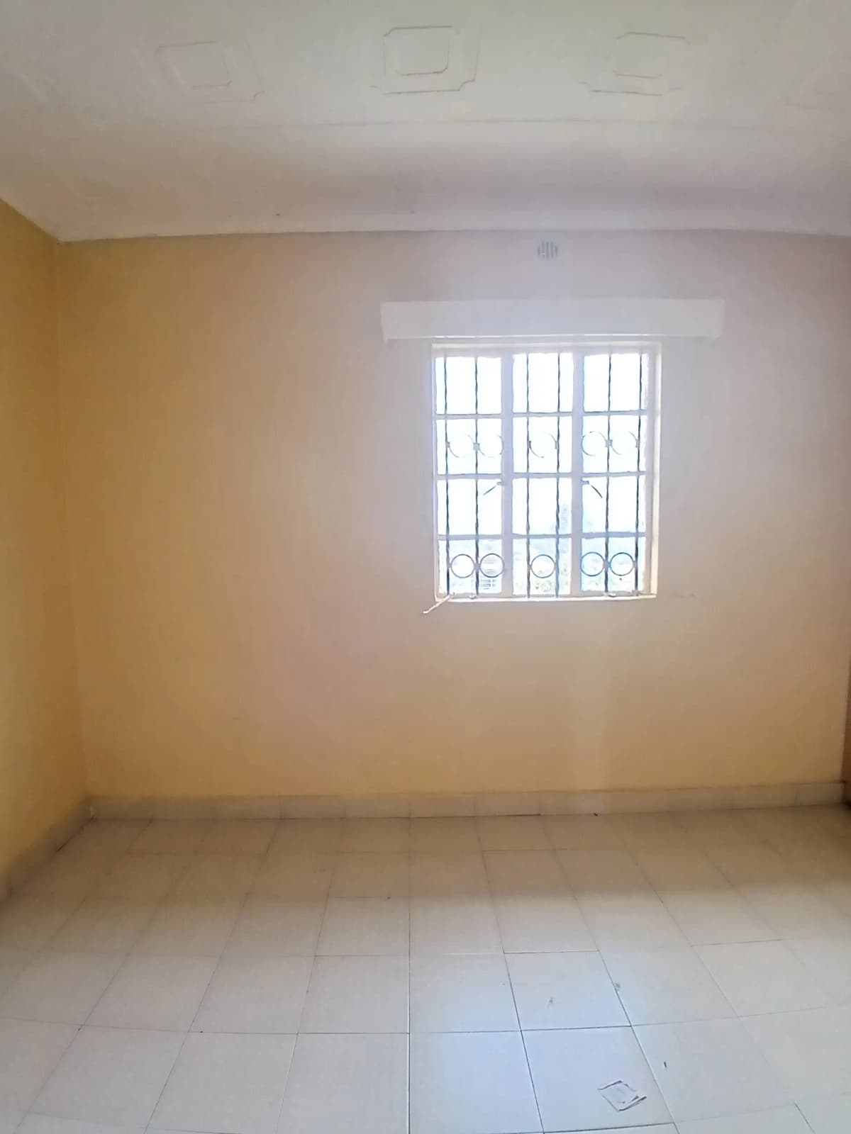 Empty bedroom with barred window and tiled flooring