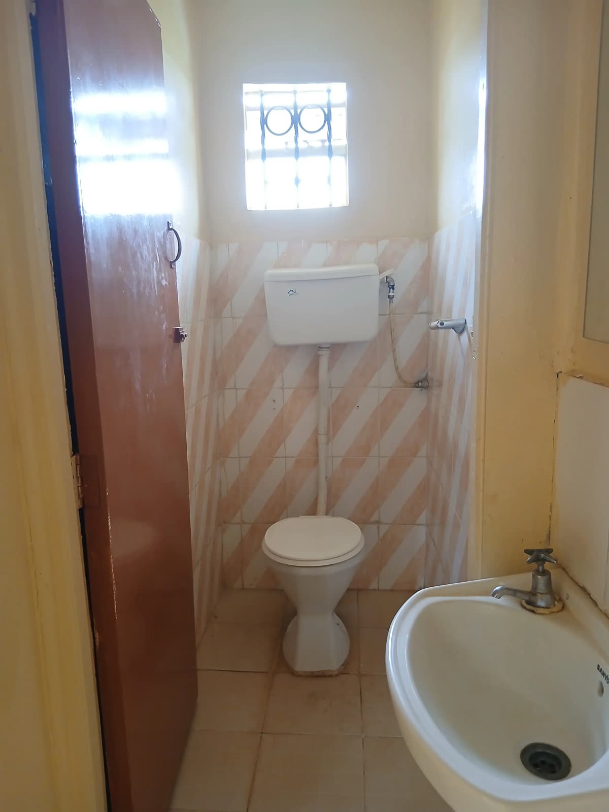 Small bathroom with toilet, sink, and window with bars