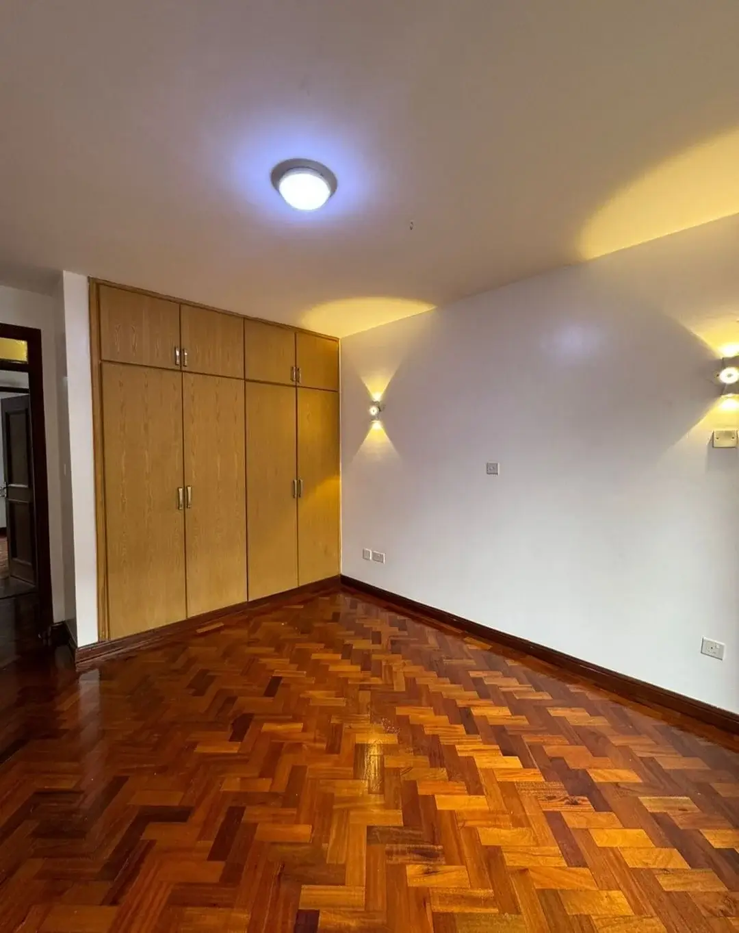 Spacious bedroom with herringbone wood flooring and built-in wardrobes