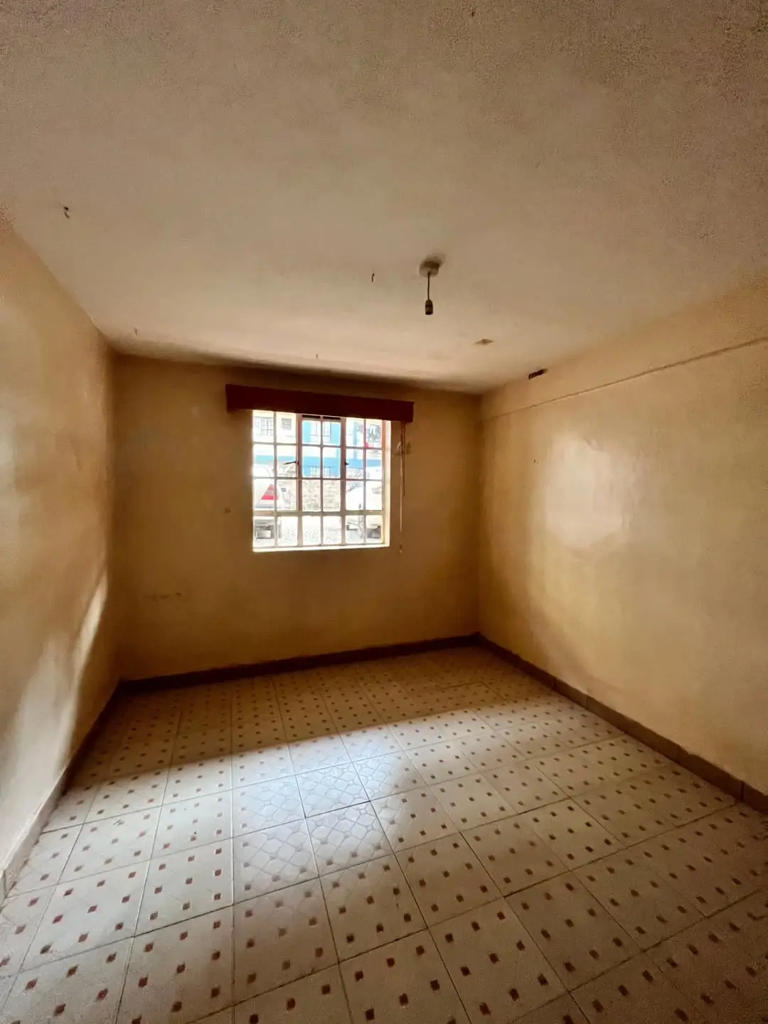 Empty bedroom with barred window and perforated tile flooring