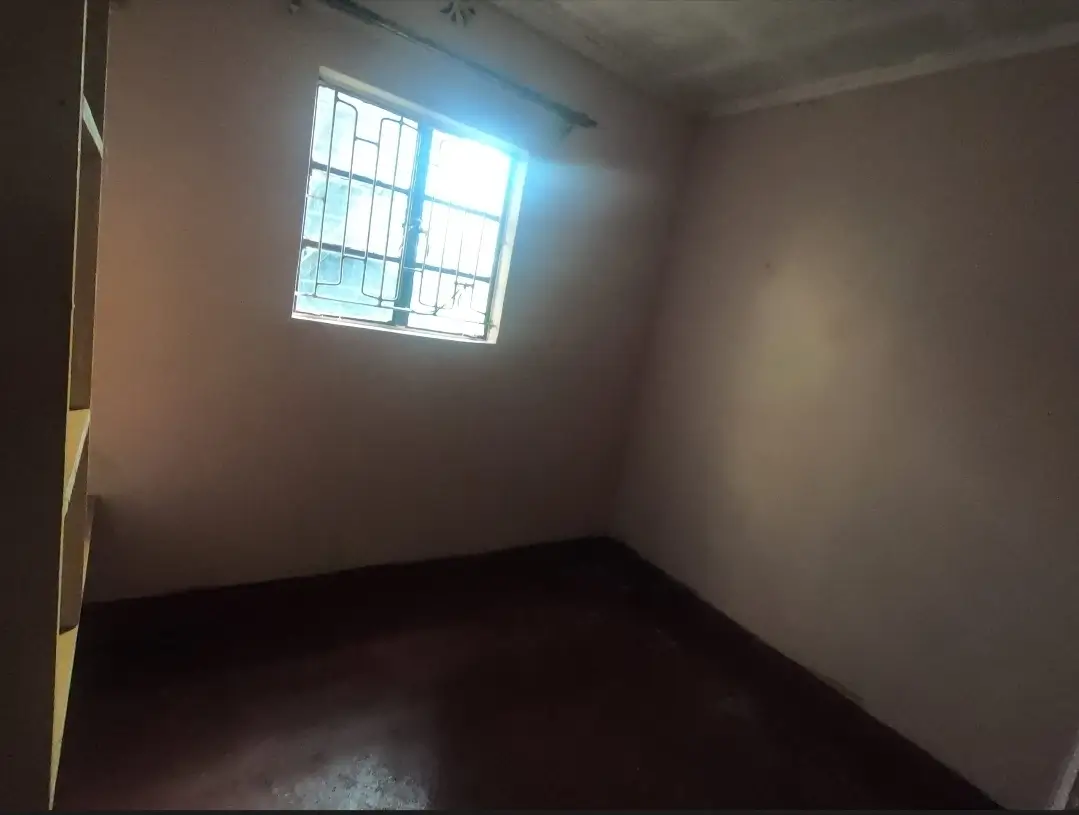Empty bedroom with barred window and dark flooring