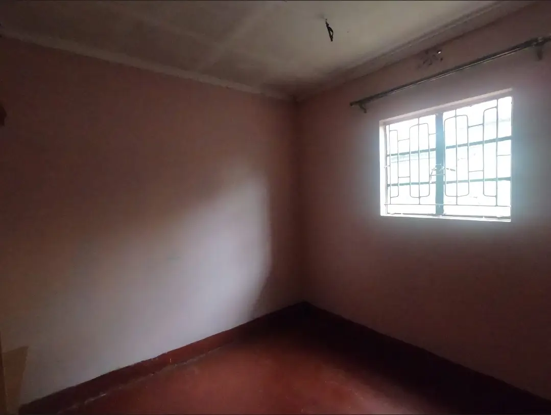 Empty bedroom with barred window and terracotta floor