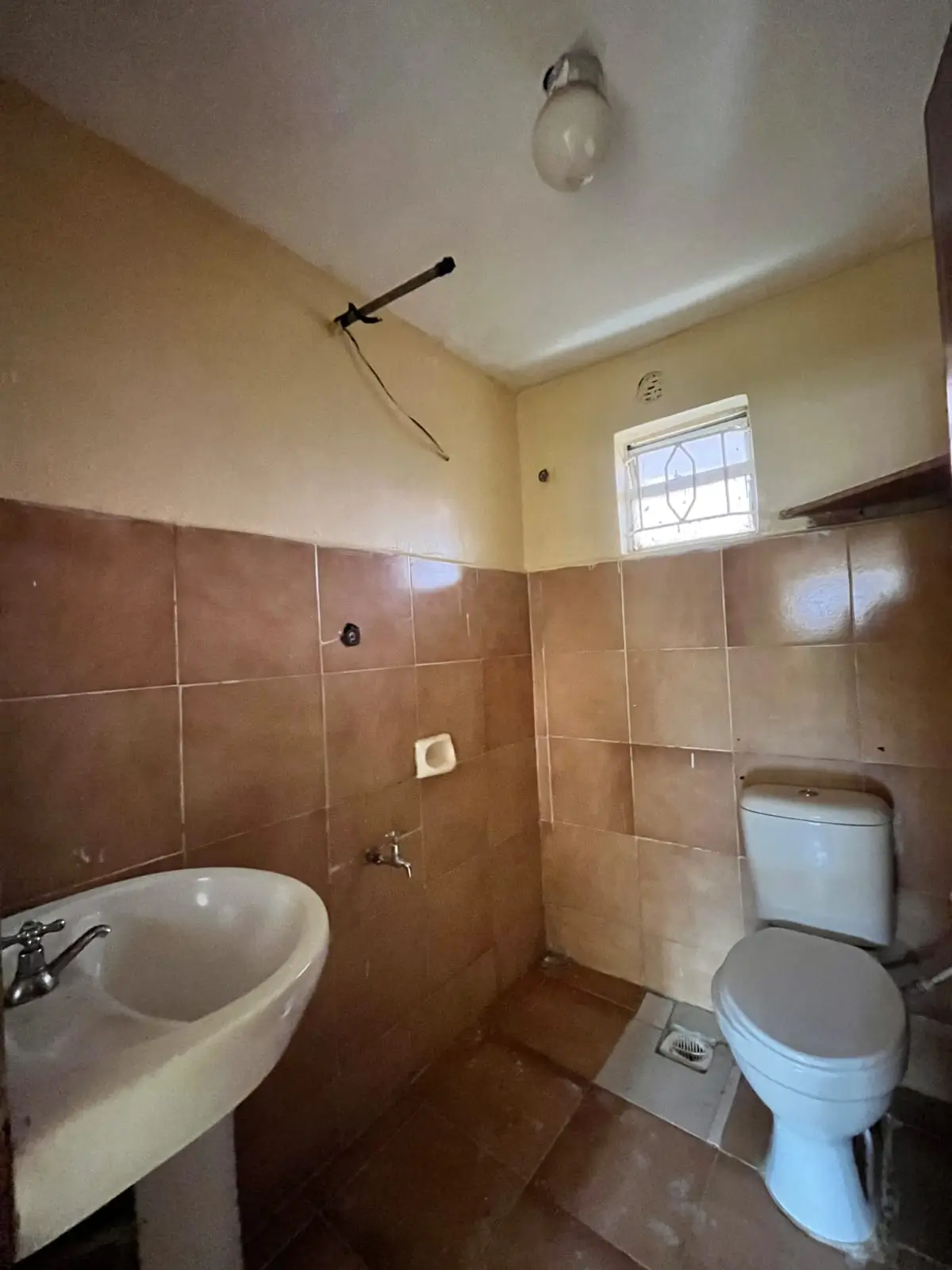Compact bathroom with basin, toilet, and brown tile walls