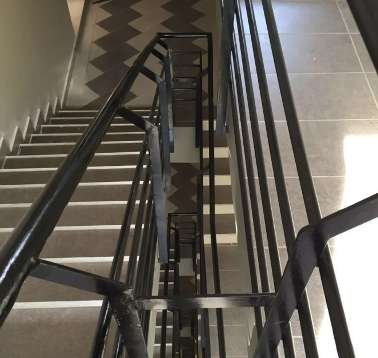 Multi-story stairwell with black railings and geometric flooring