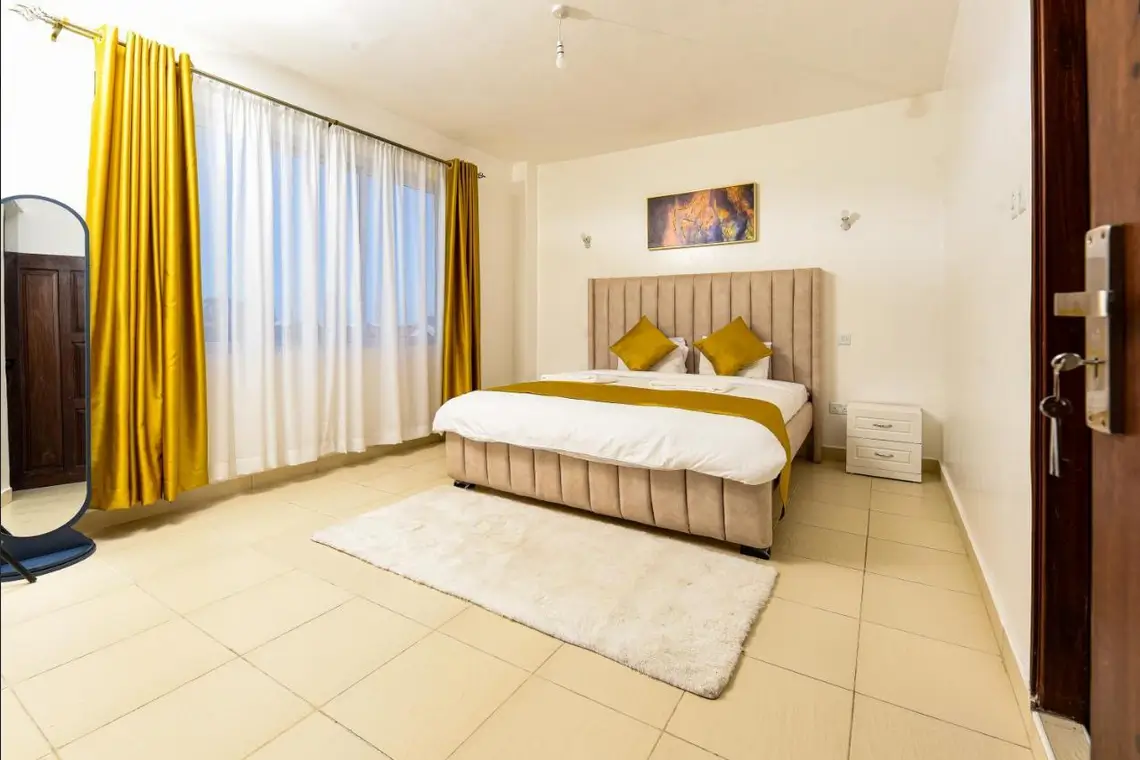 Master bedroom with upholstered bed, golden curtains, large windows