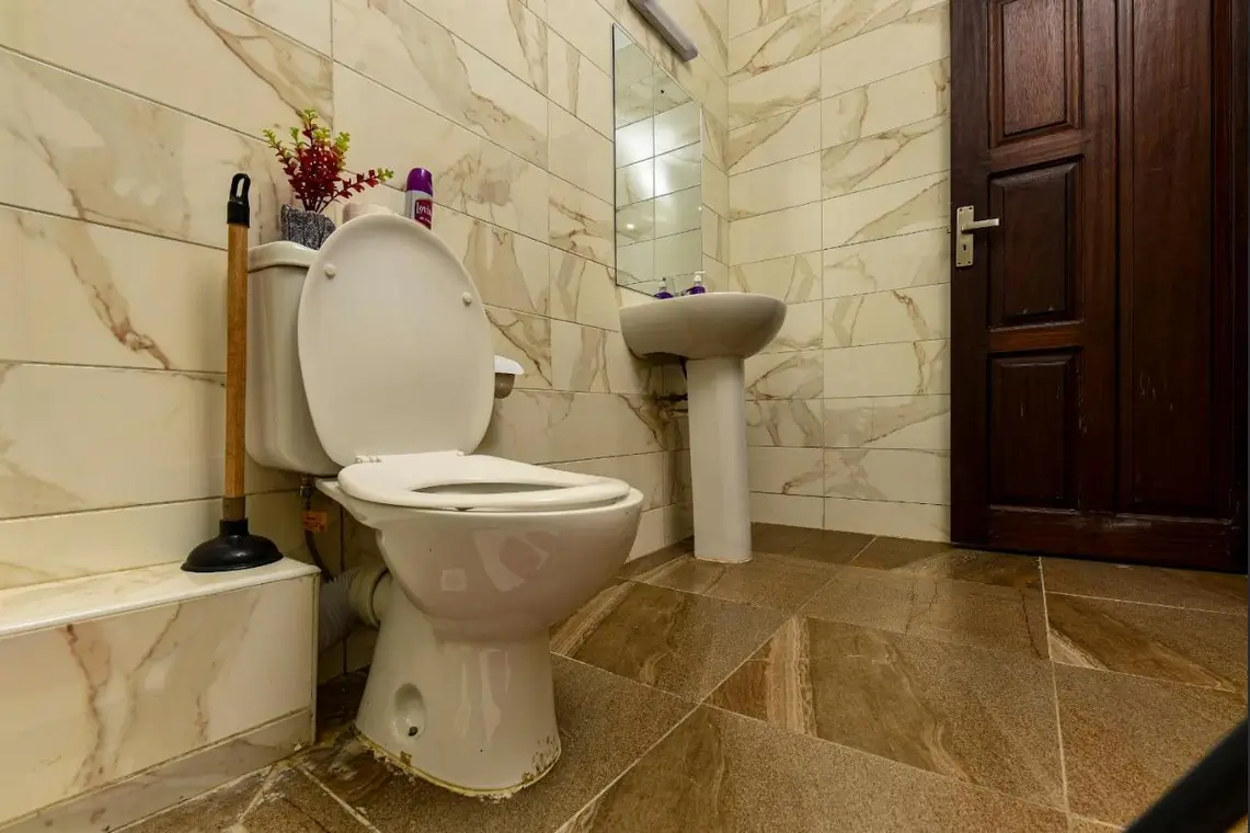 Marble-tiled bathroom with toilet, pedestal sink, and wooden door