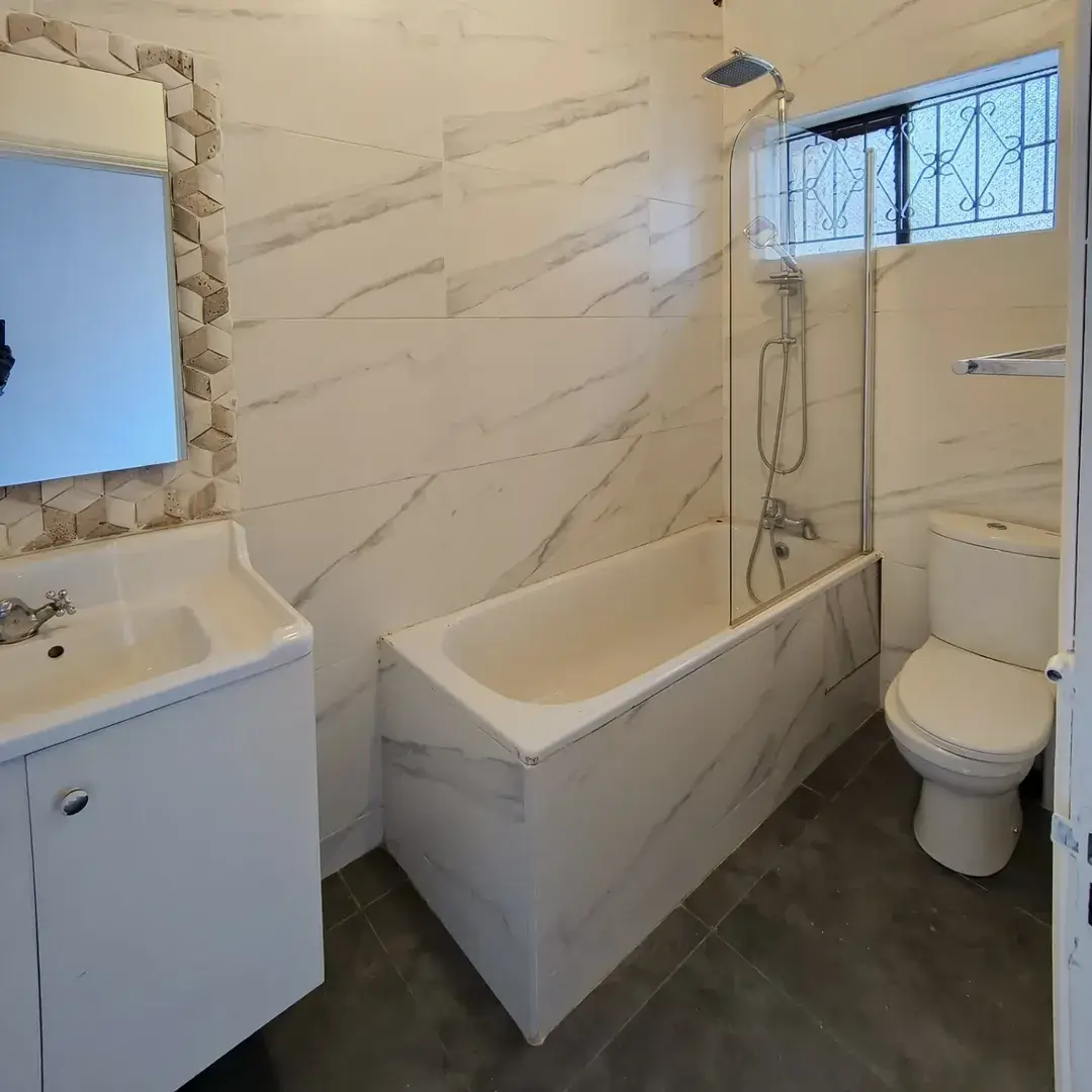 Modern bathroom with marble tiles, bathtub, and glass shower enclosure