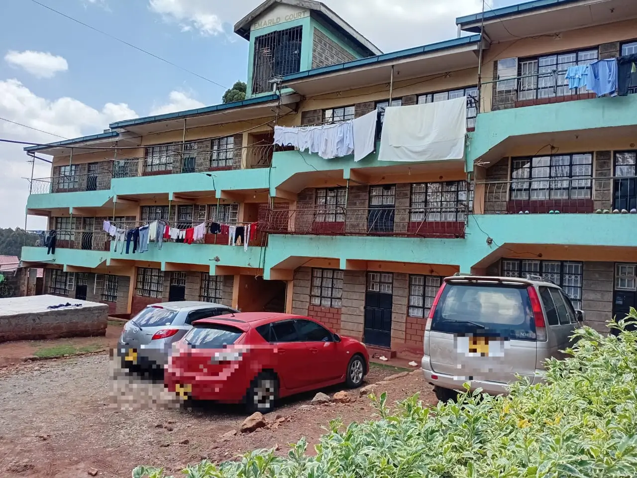 Multi-story residential building with turquoise trim and parked vehicles