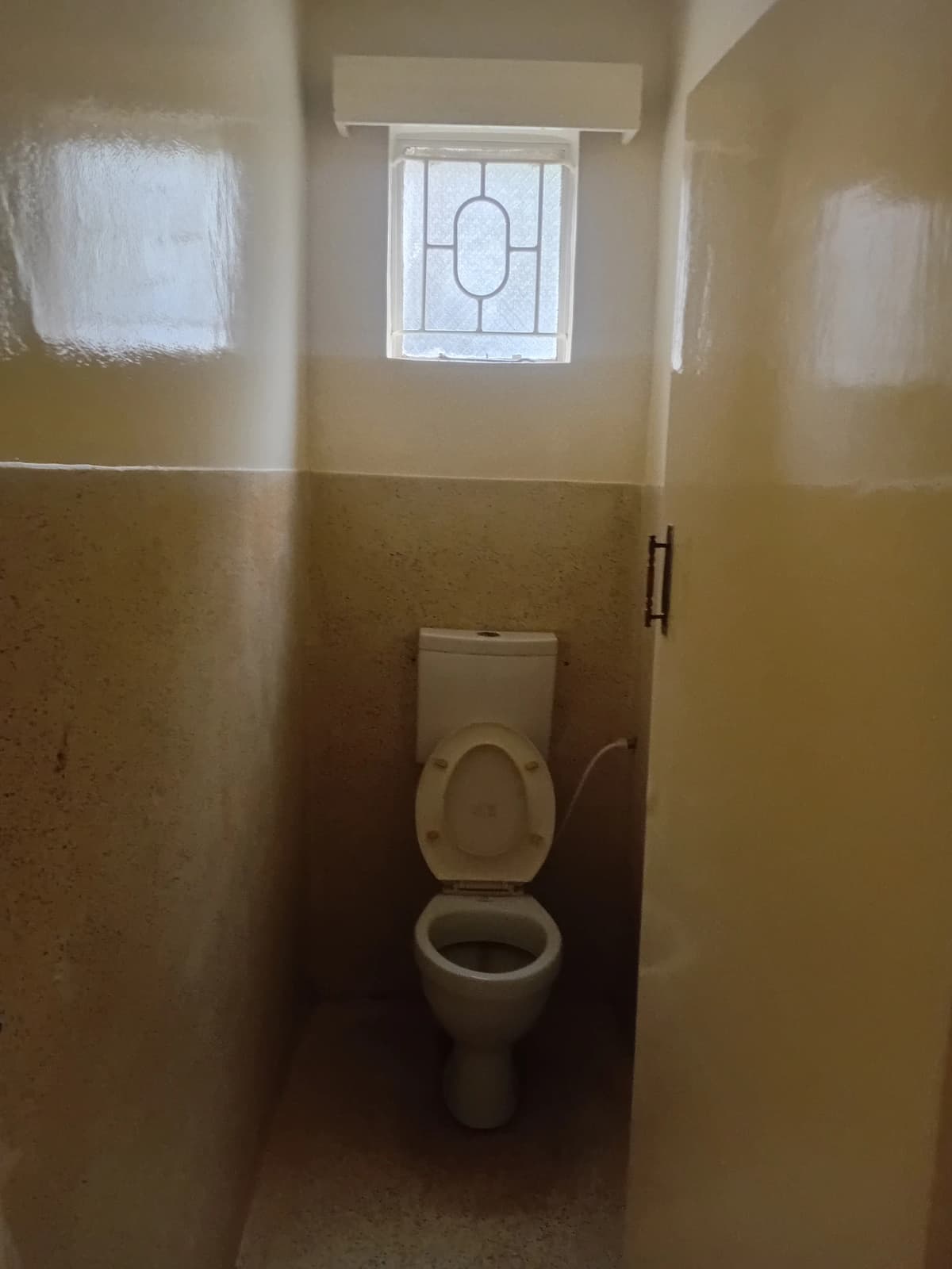 Toilet cubicle with half-tiled walls and small window