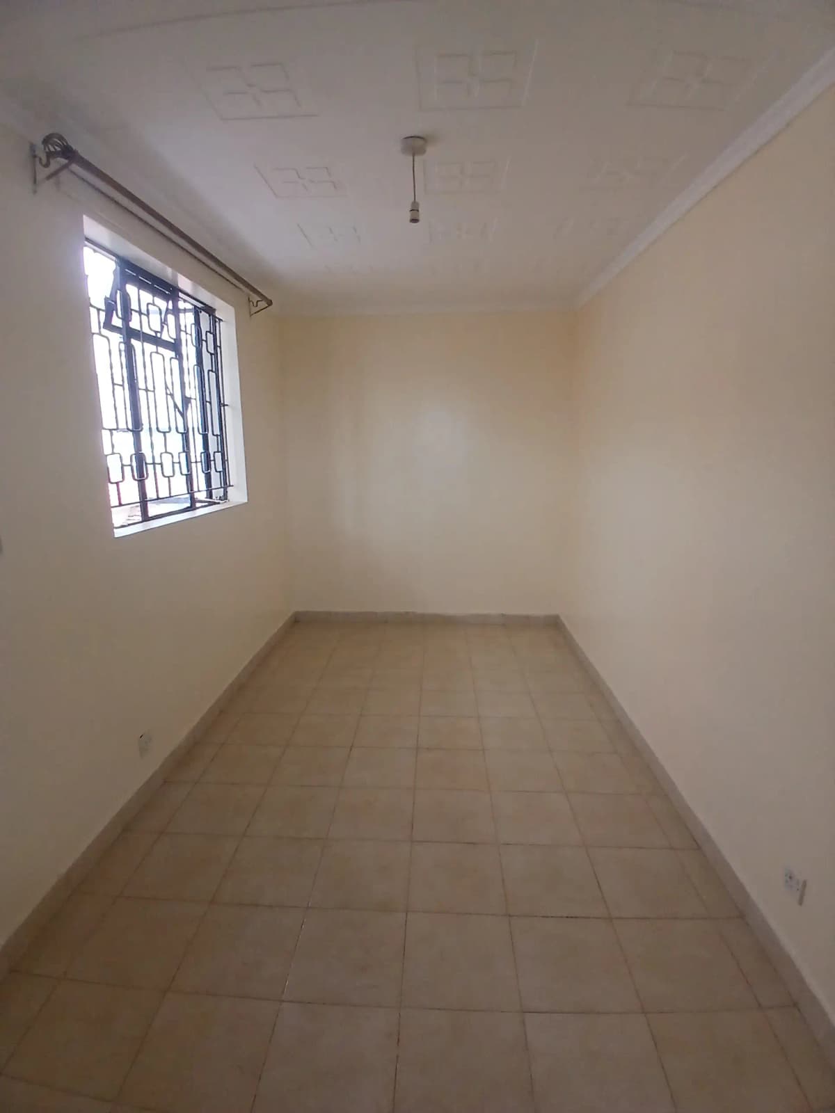 Empty bedroom with barred window and tiled flooring