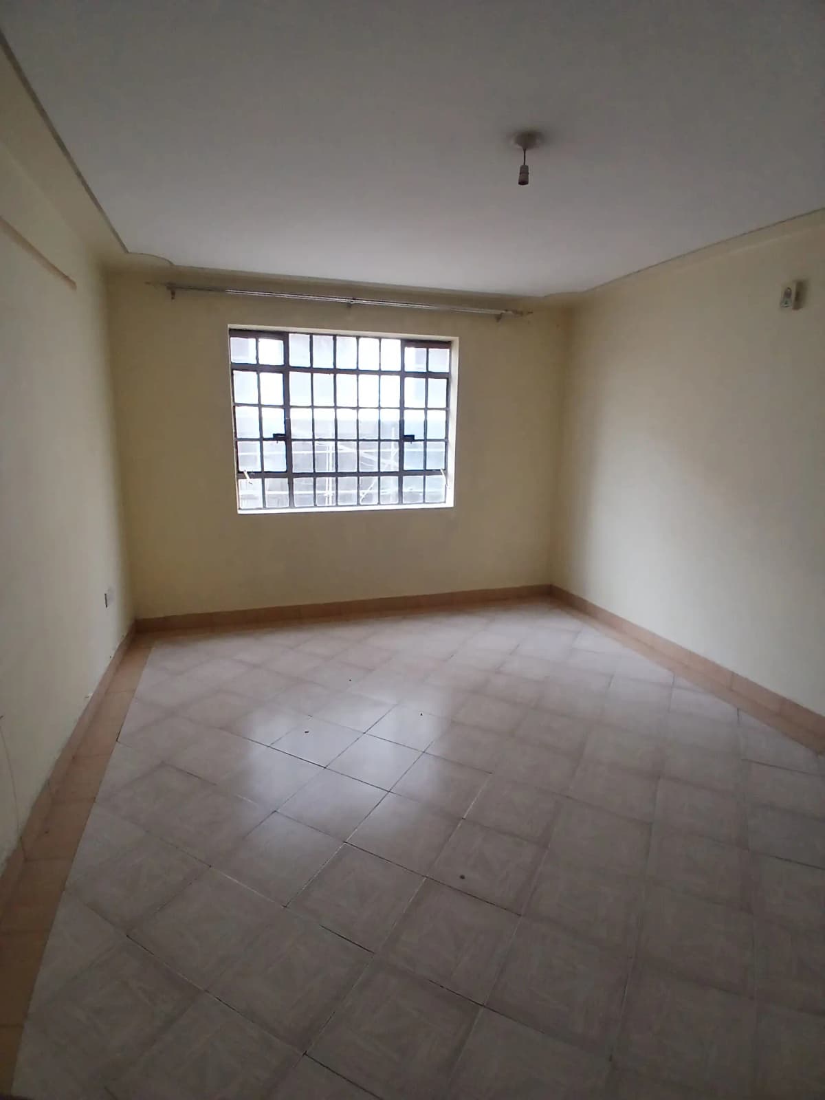 Spacious bedroom with barred window and tiled flooring
