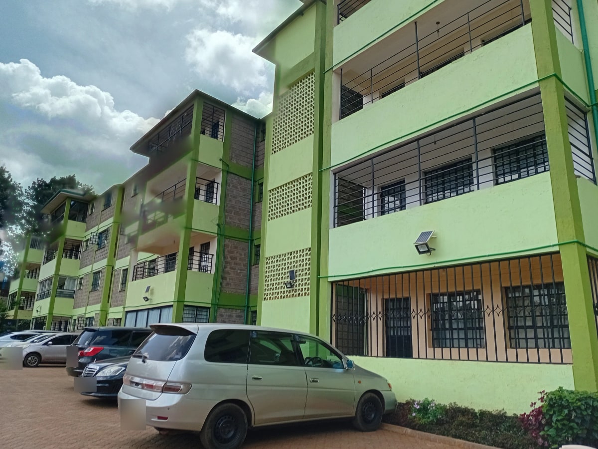Multi-story residential building with green facade and parking area