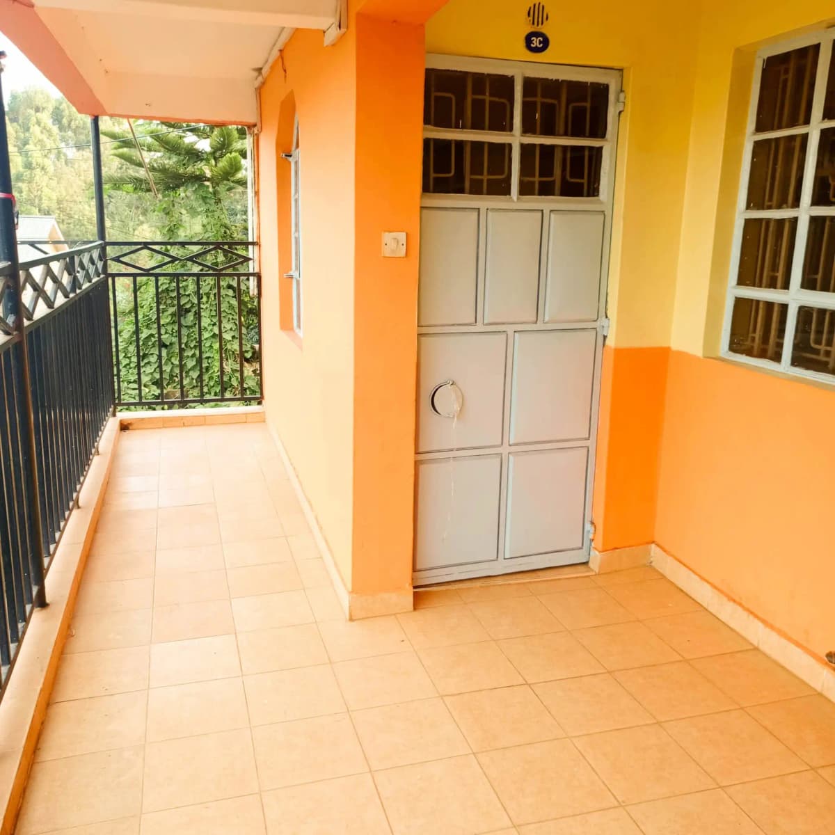 Covered balcony with orange pillars and railing overlooking greenery