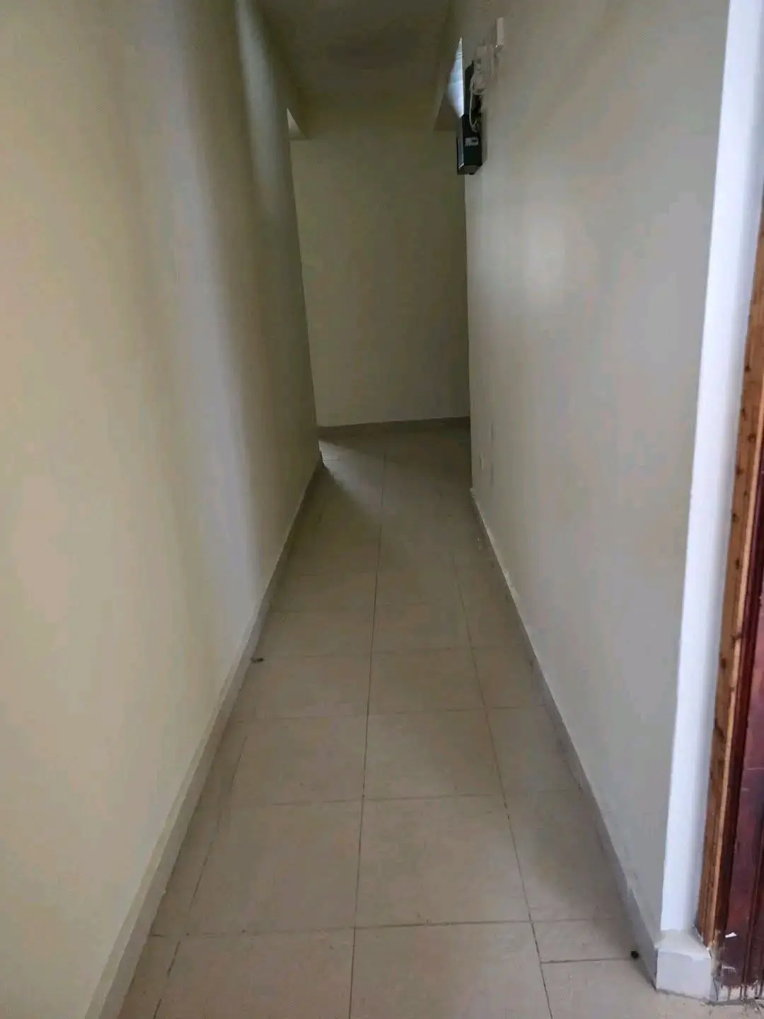 Narrow interior corridor with tiled flooring and plain walls