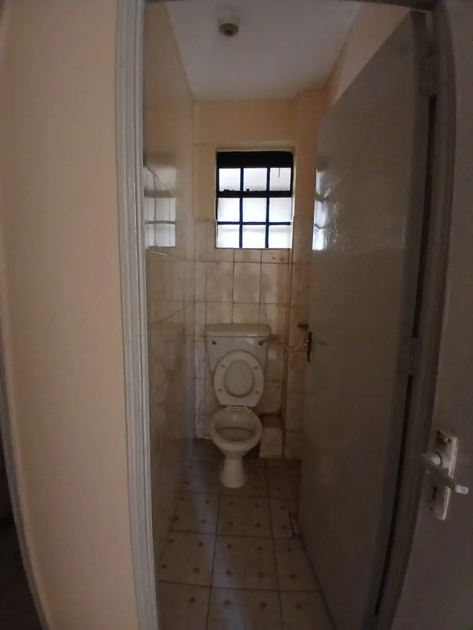 Narrow bathroom with toilet and window, tiled flooring