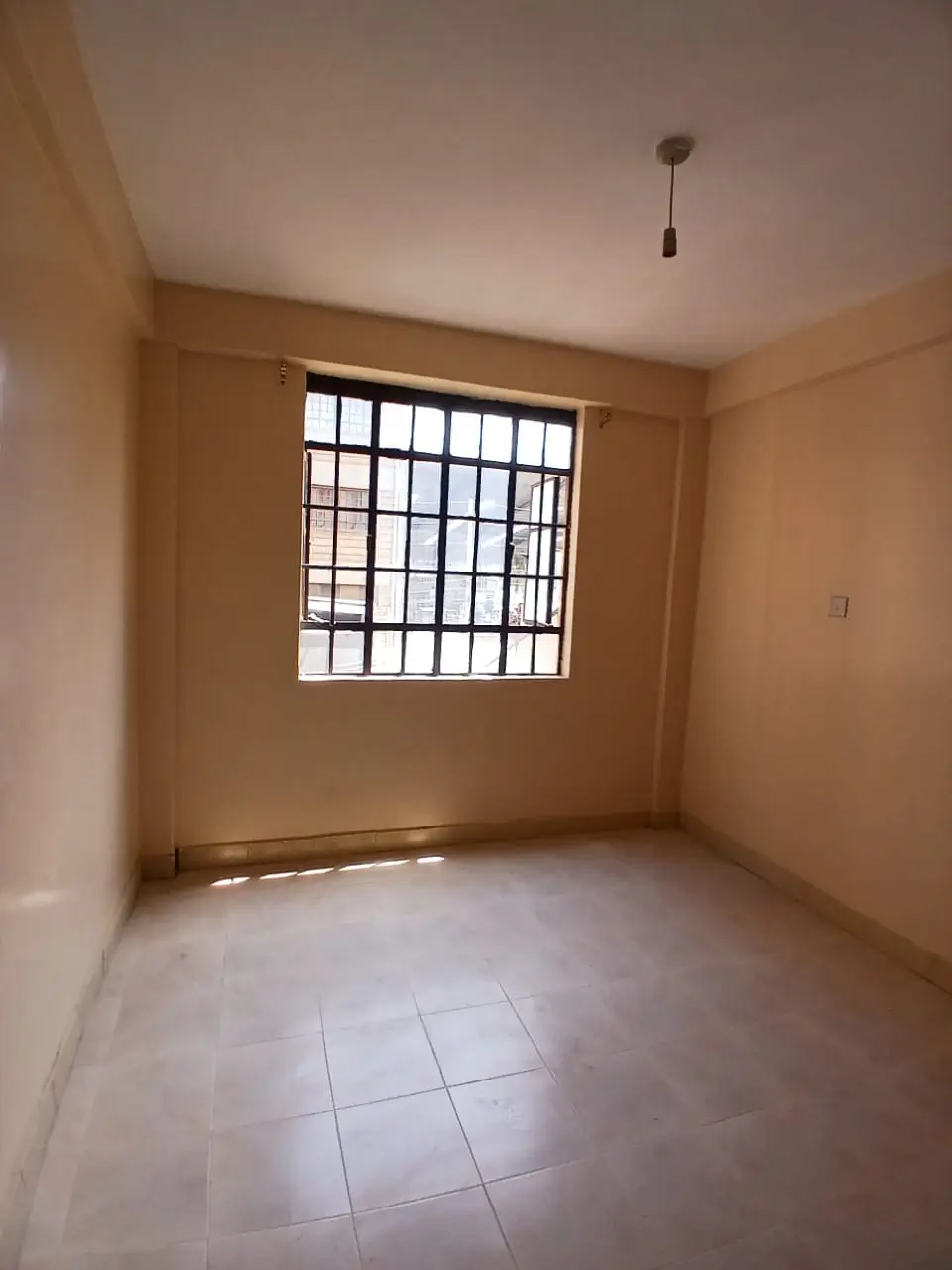 Bare bedroom with barred window, tiled floor, minimal furnishings