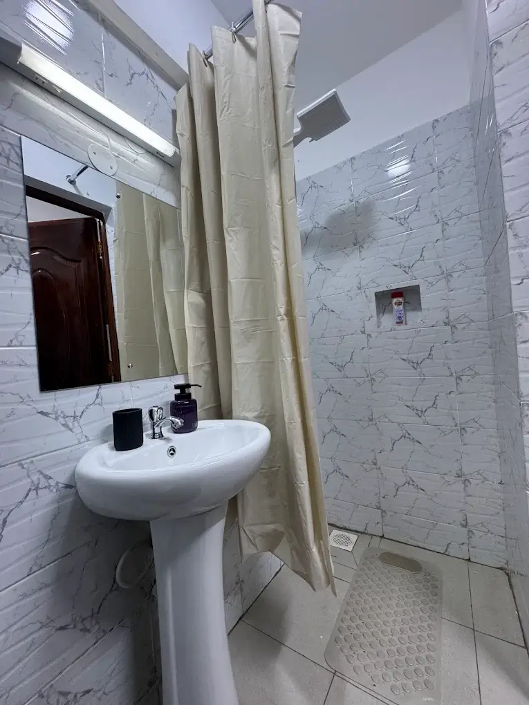 White marble-tiled bathroom with pedestal sink and shower curtain