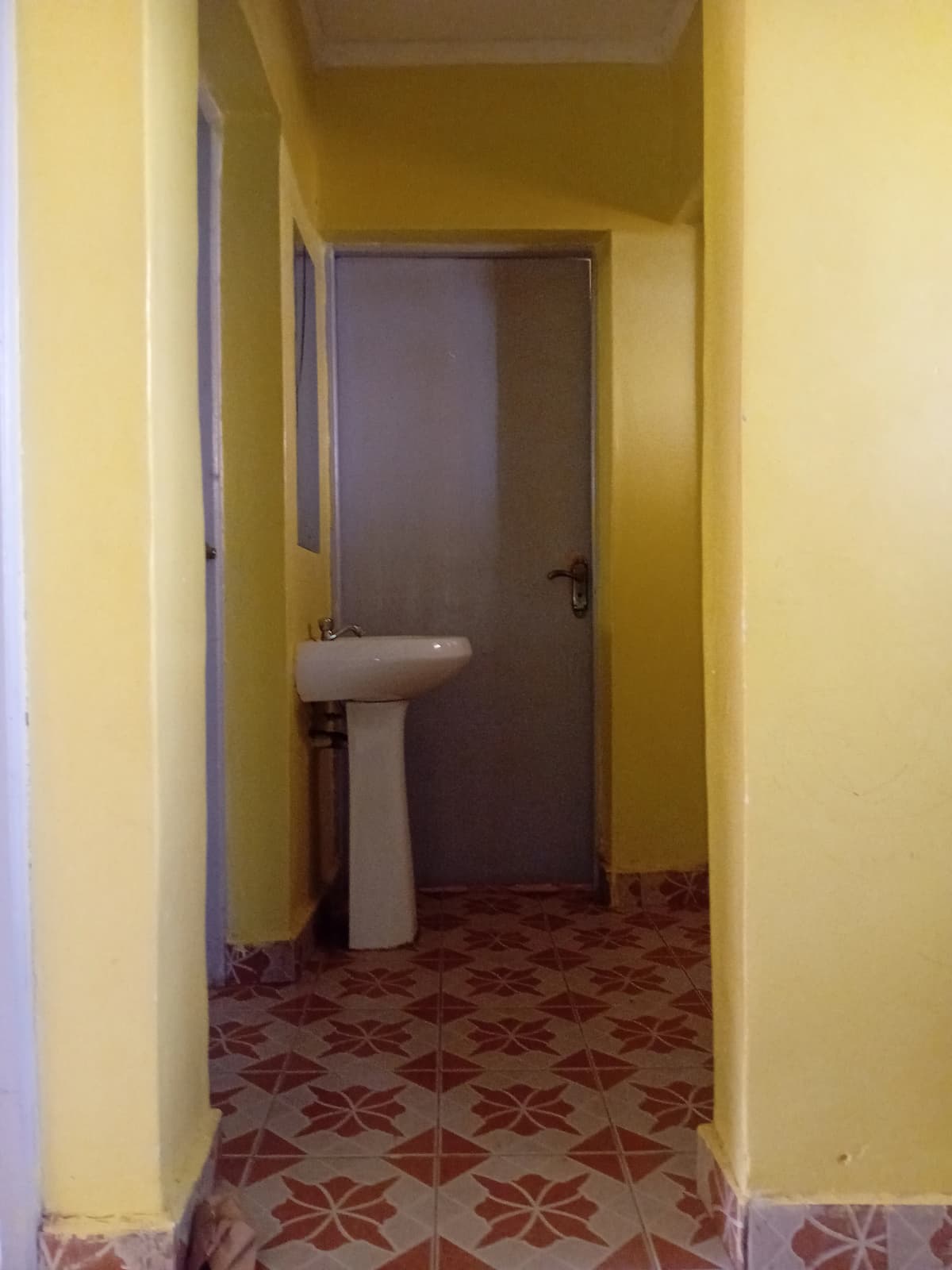 Yellow corridor leading to bathroom with pedestal sink