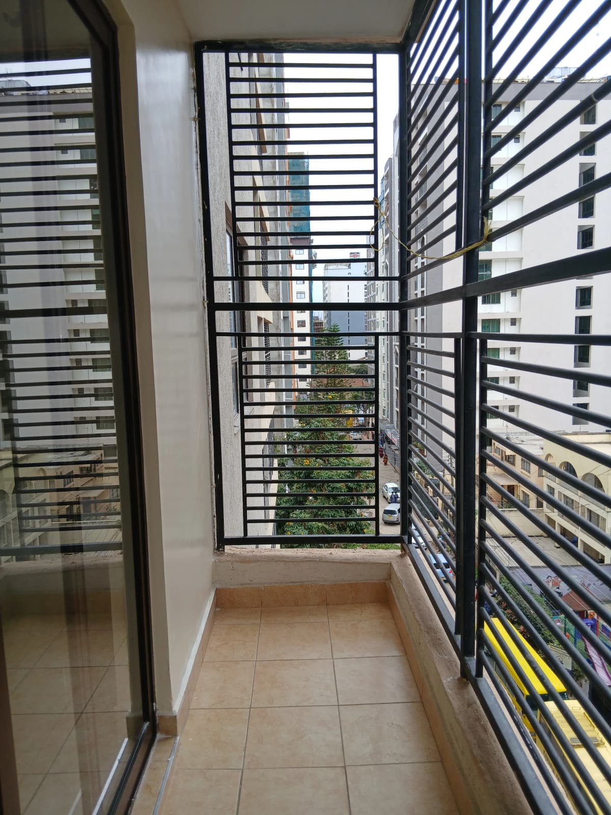 Narrow balcony with black louvered railings and city views