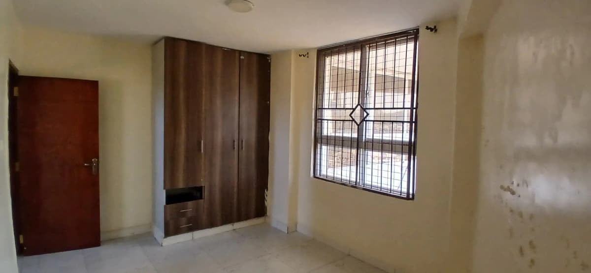 Unfurnished bedroom with wooden wardrobes and barred window
