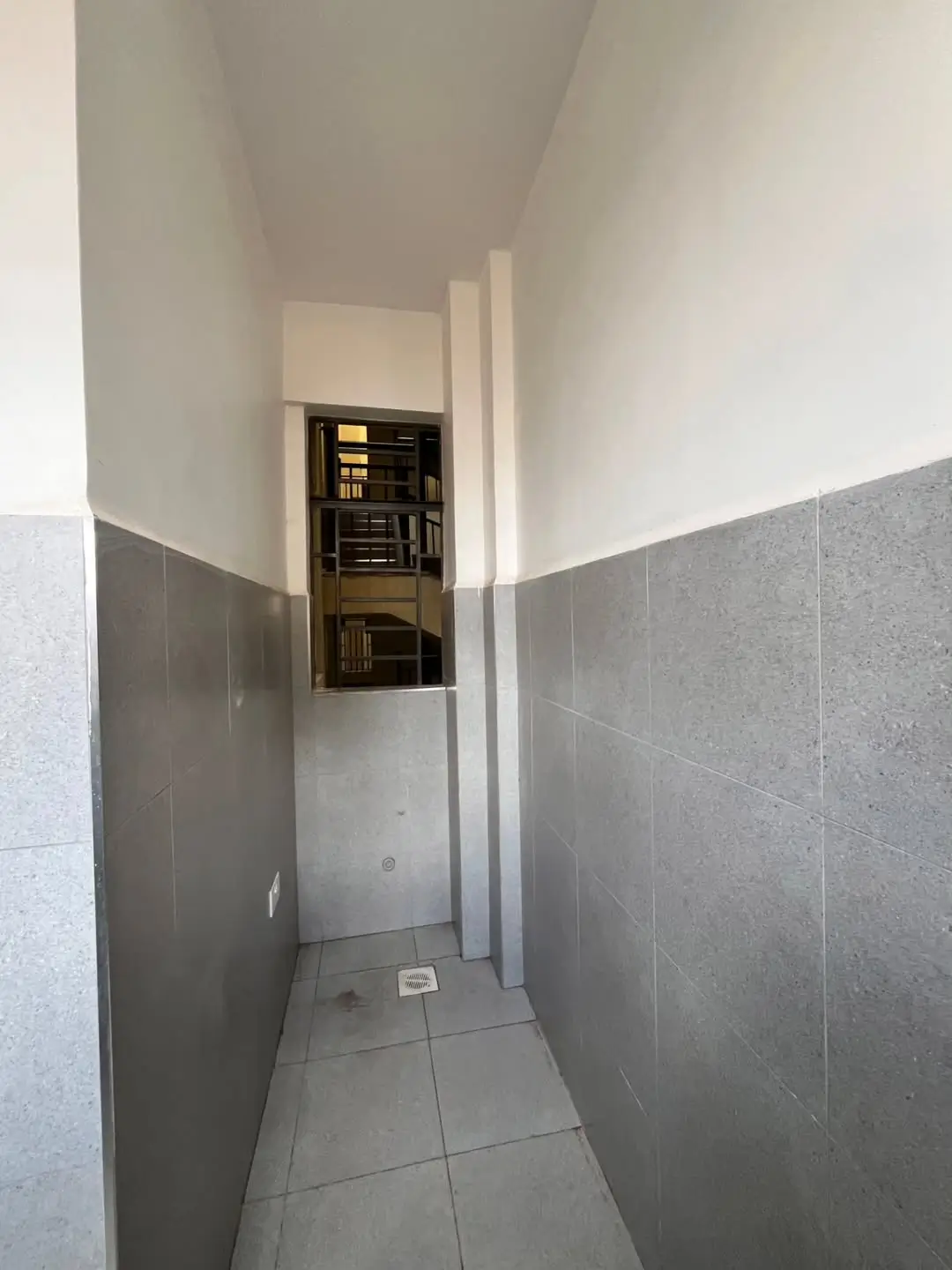 Narrow hallway with grey tile walls and built-in storage
