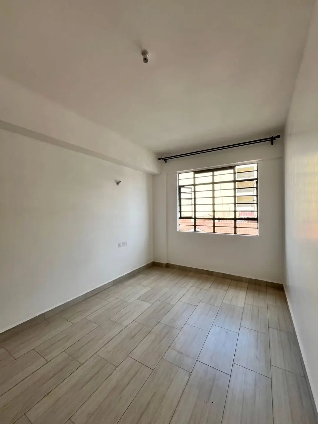 Unfurnished bedroom with barred window and tiled flooring
