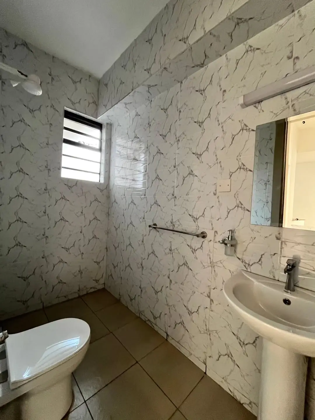 Bathroom with marble-patterned tiles, pedestal sink, toilet