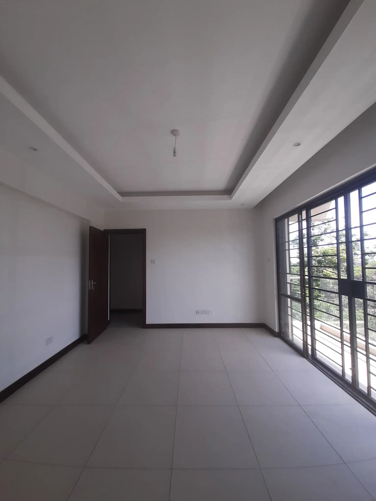 Spacious empty living room with tiled flooring and barred windows