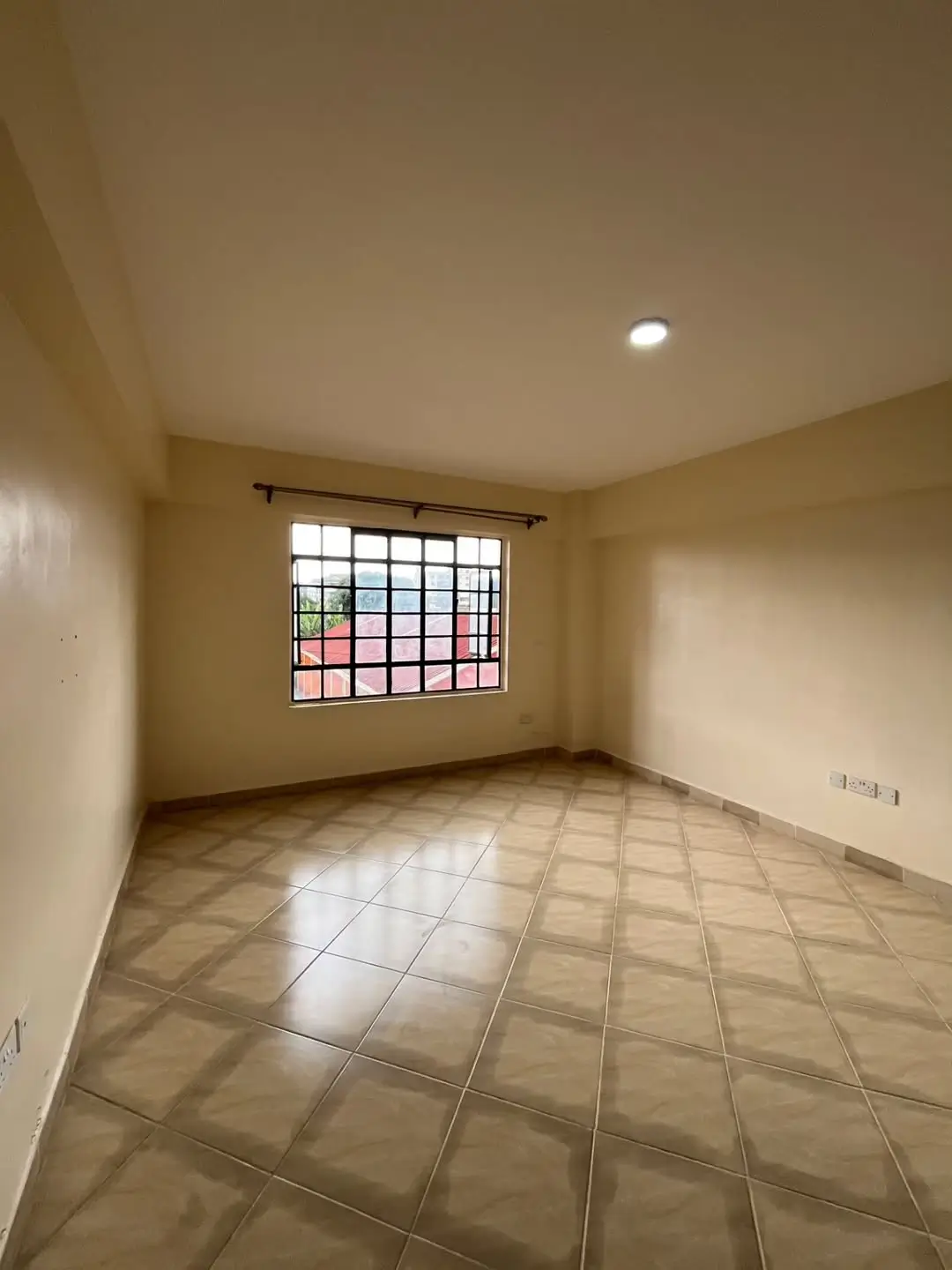 Spacious bedroom with tiled flooring and barred window