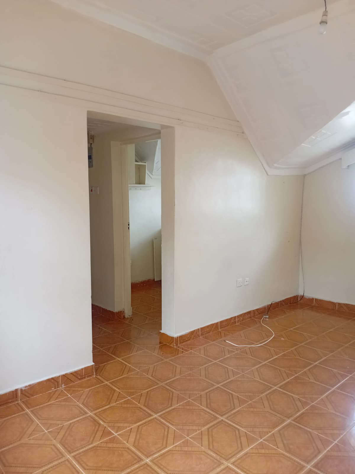 Vacant bedroom with terracotta tile flooring and sloped ceiling