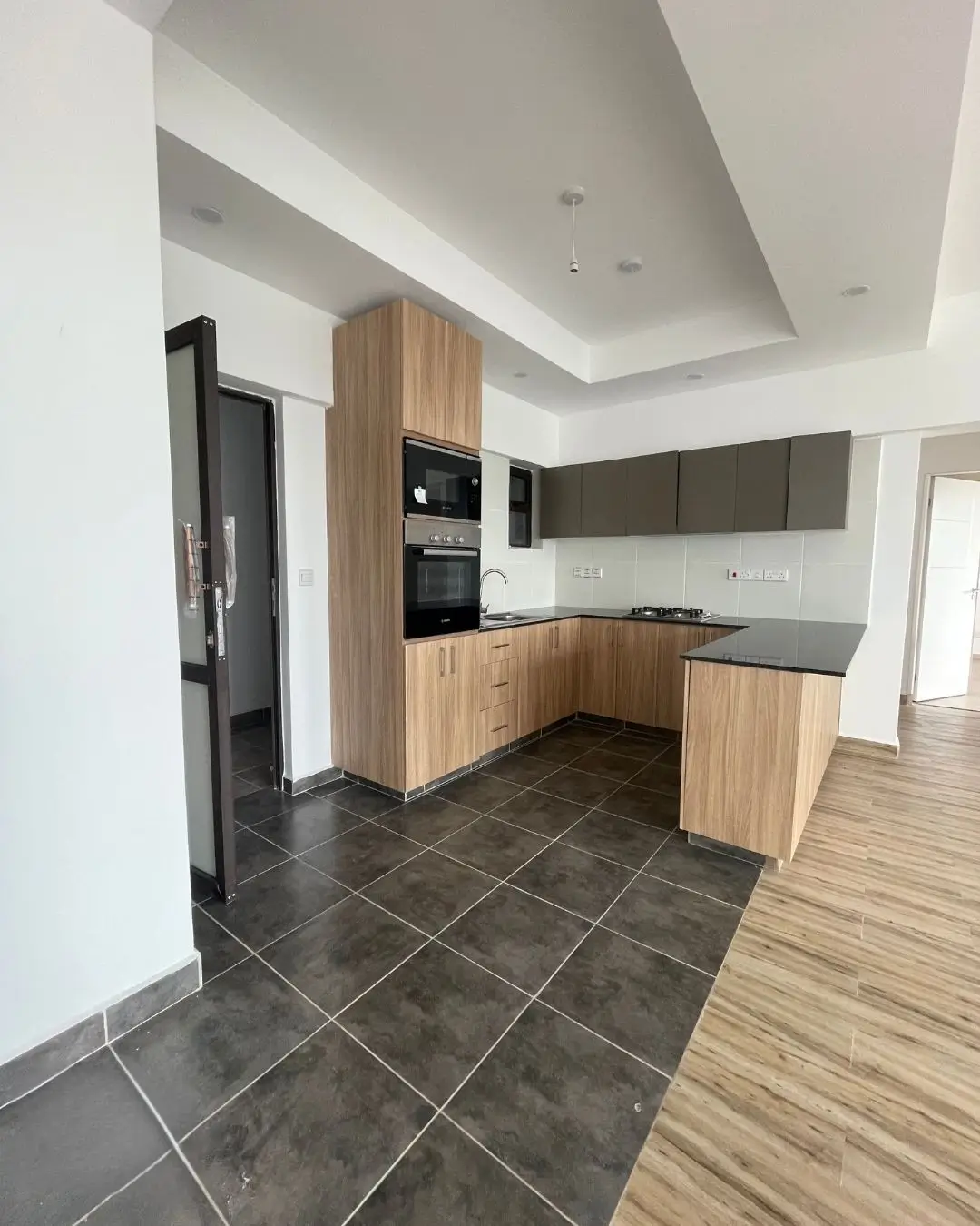 Modern kitchen with wood cabinetry, dark tile flooring, built-in appliances