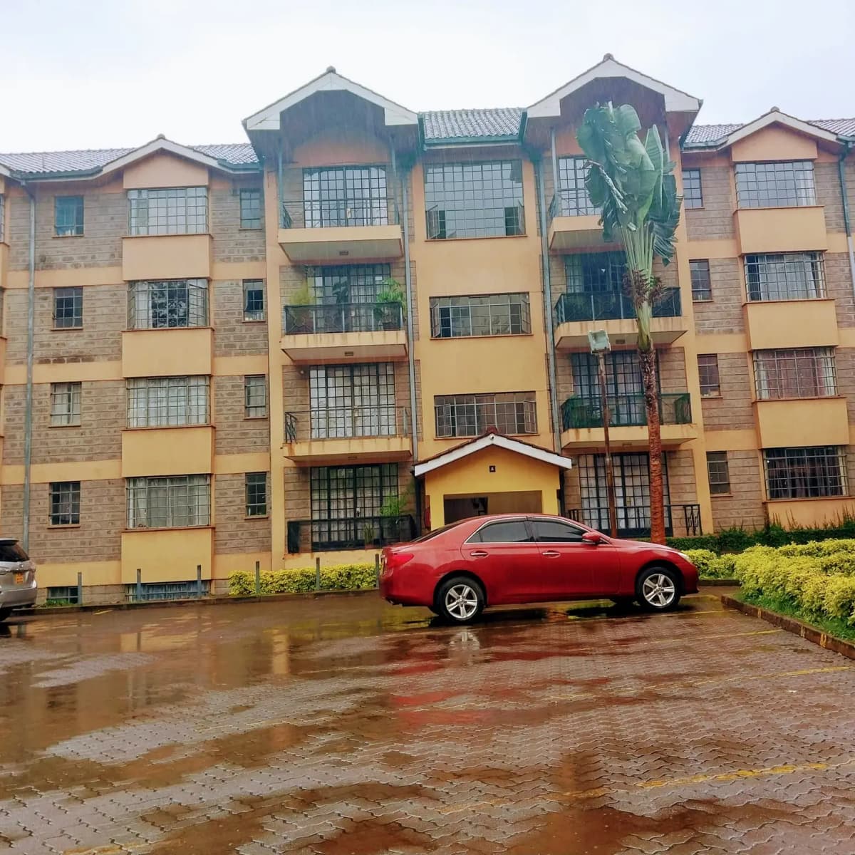 Multi-story residential building facade with parked red car