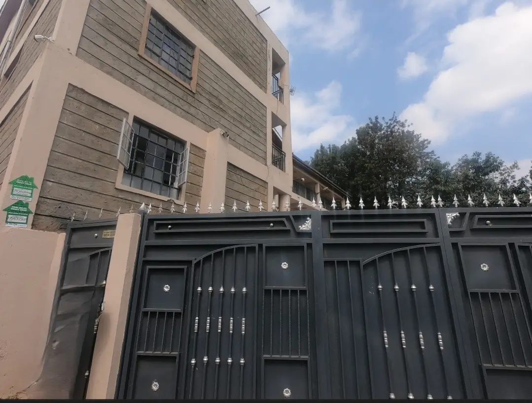 Multi-story residential building with black metal gate and compound.