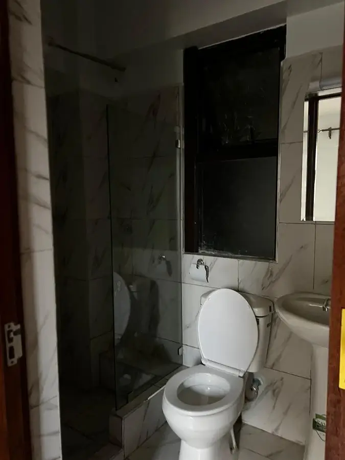 Compact bathroom with toilet, sink, and glass shower enclosure