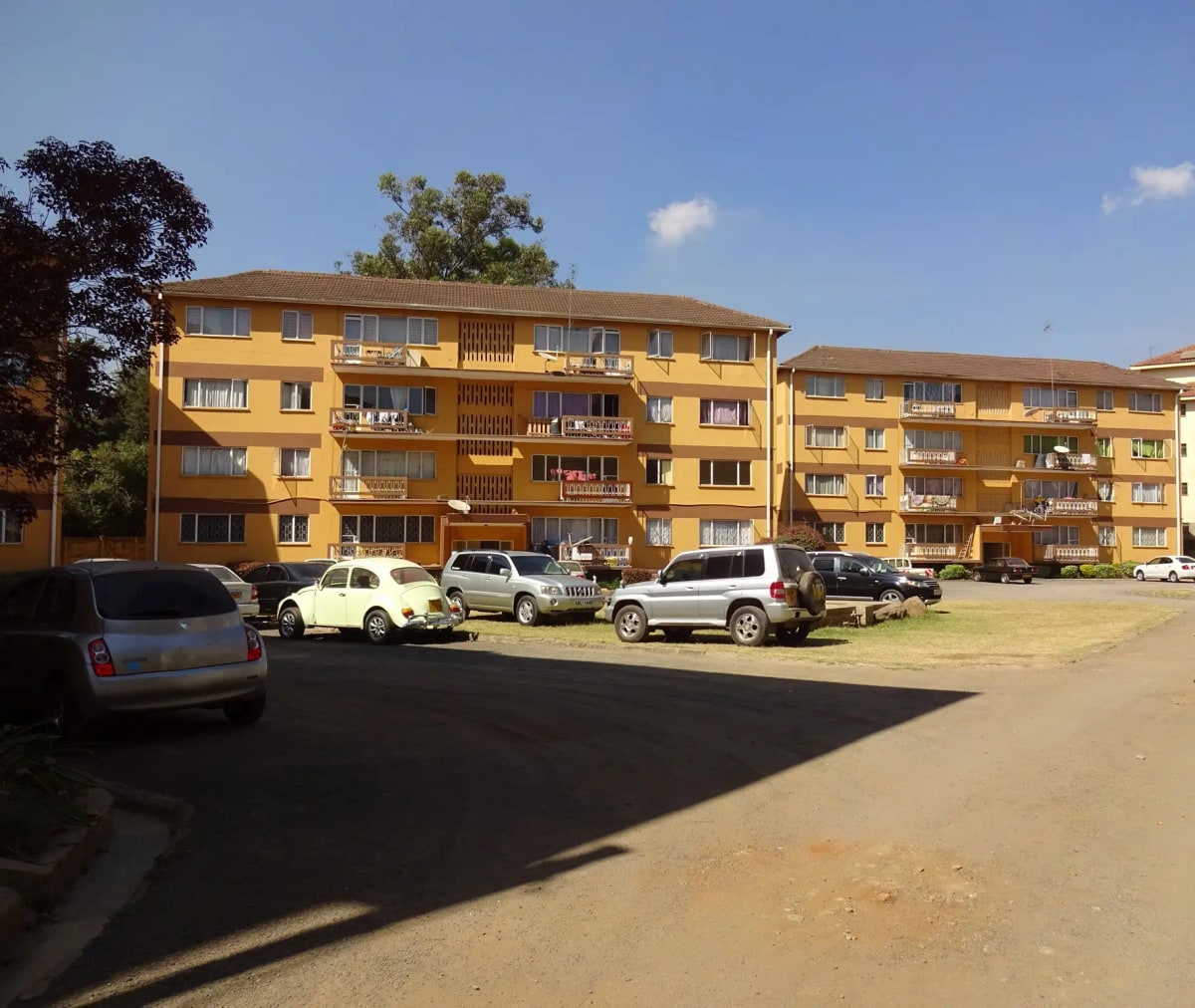 Yellow apartment building facade with parking lot and vehicles