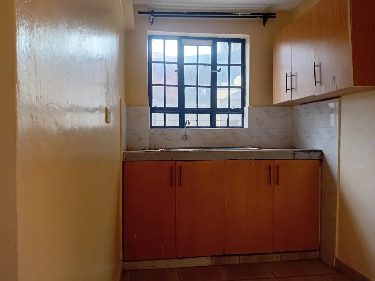 Compact kitchen with red cabinetry and barred window