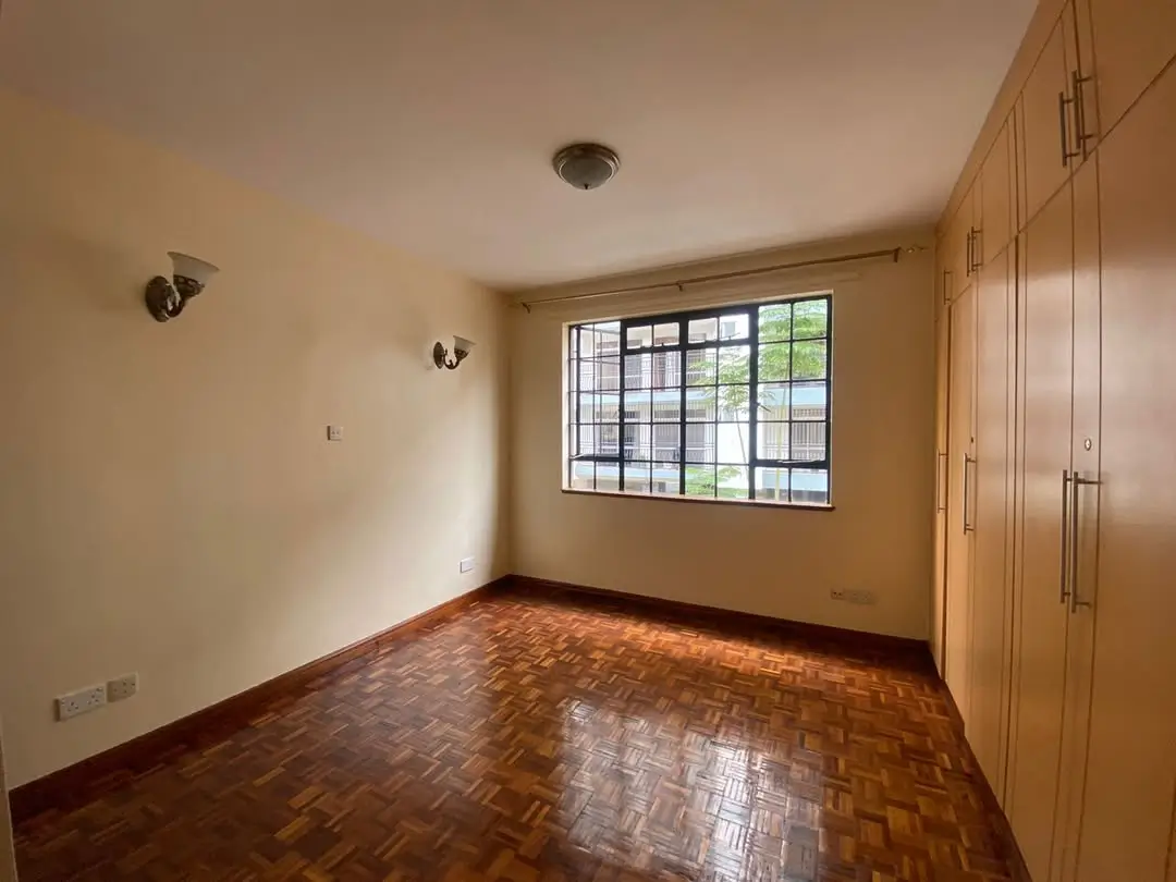 Spacious bedroom with wooden herringbone floor and built-in wardrobes