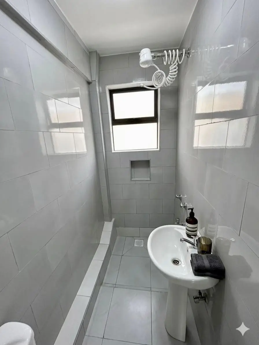 Clean white-tiled bathroom with pedestal sink and window