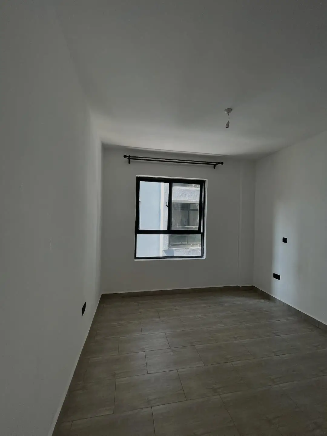 Empty bedroom with window, bare wooden floor, minimal fixtures