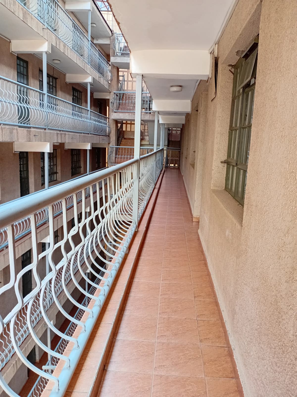 Long shared balcony with white railings, multi-story apartment building