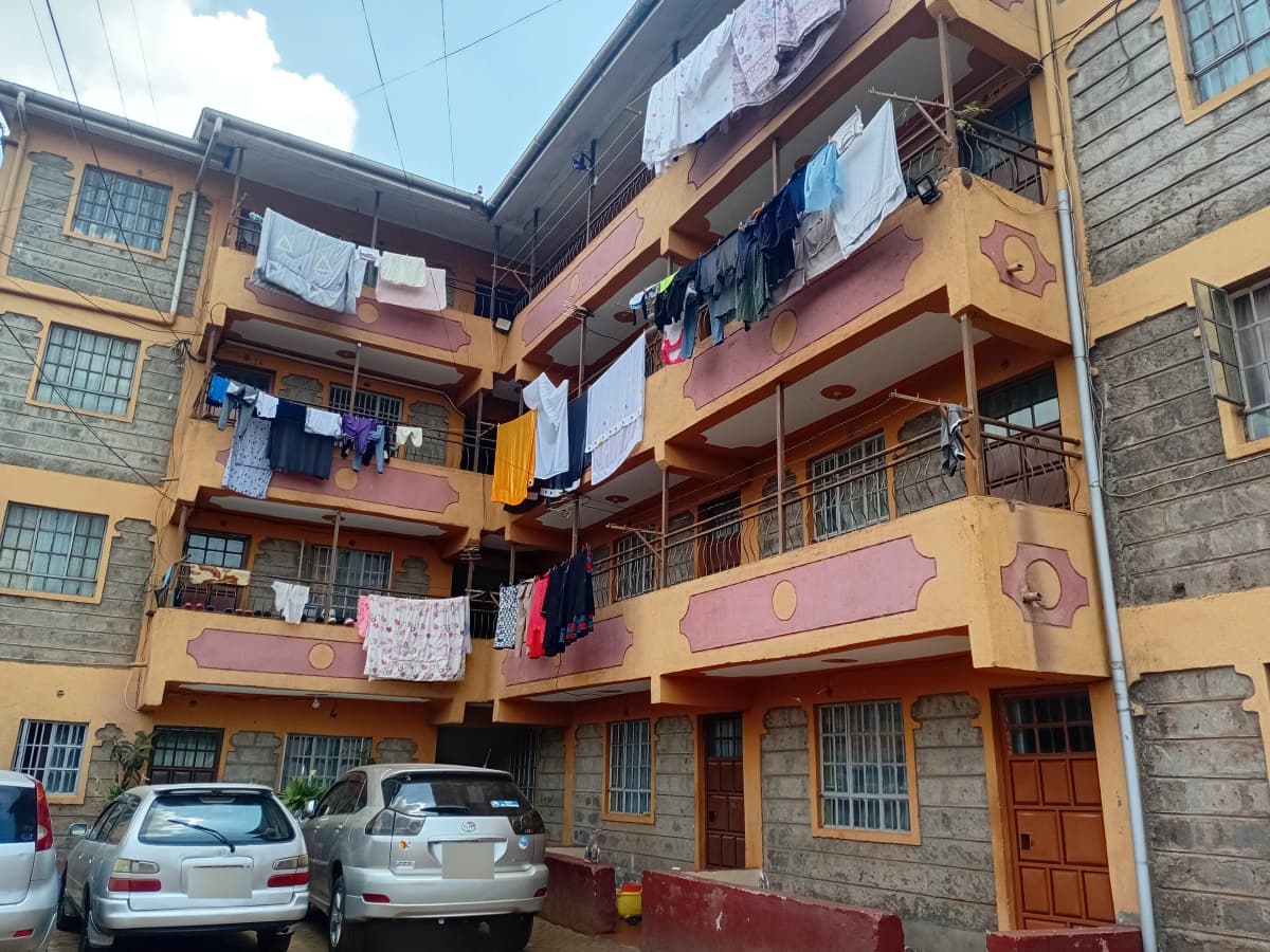 Multi-story residential building with yellow facade and parked vehicles