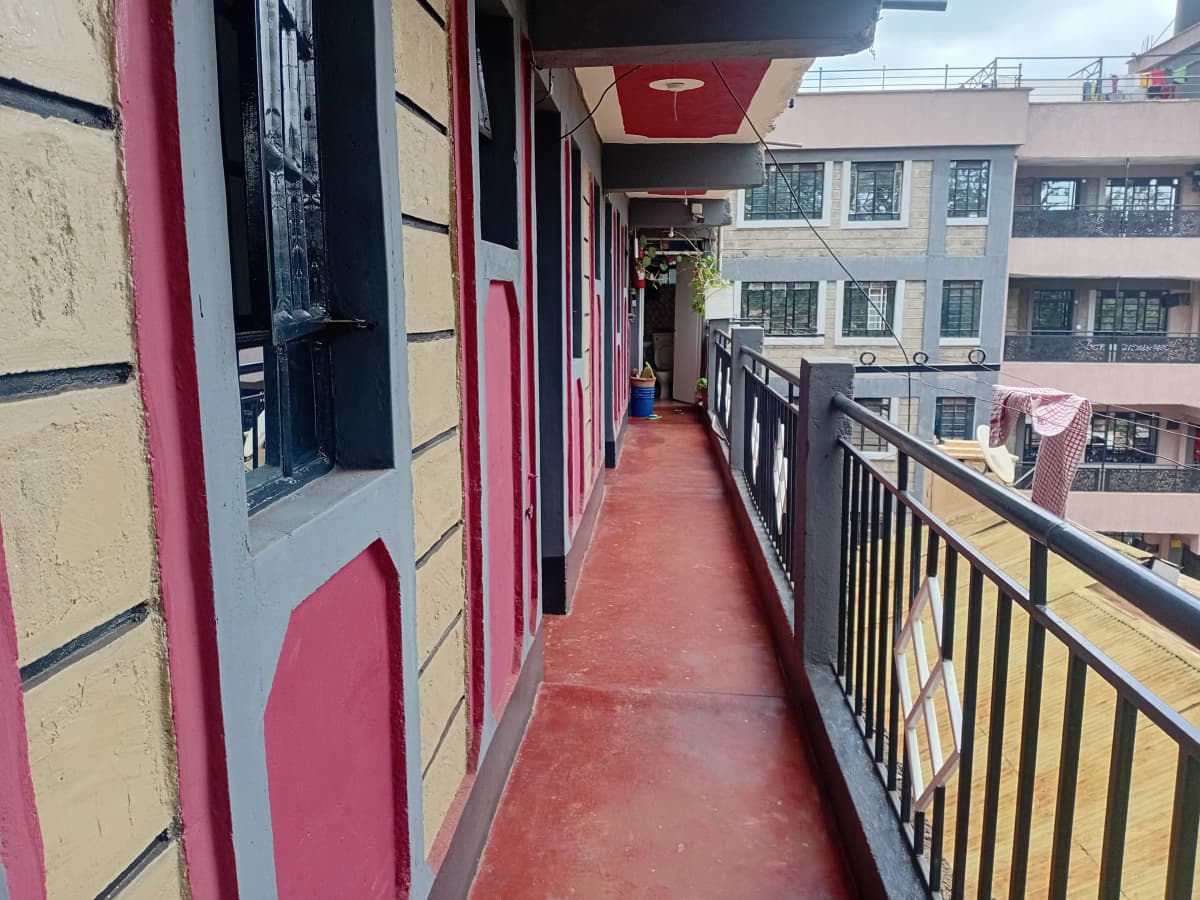 Red-floored balcony with black railings overlooking residential buildings