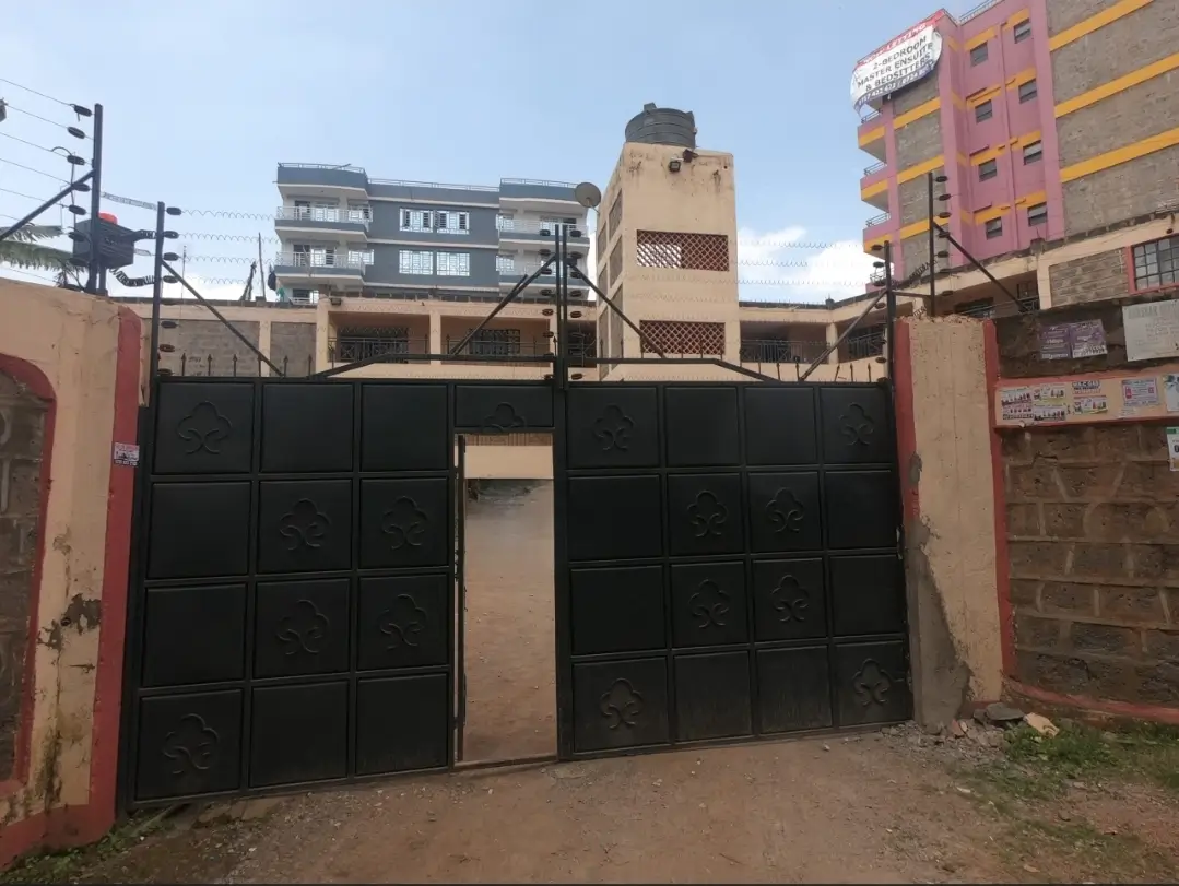 Black metal gate compound entrance with surrounding buildings visible