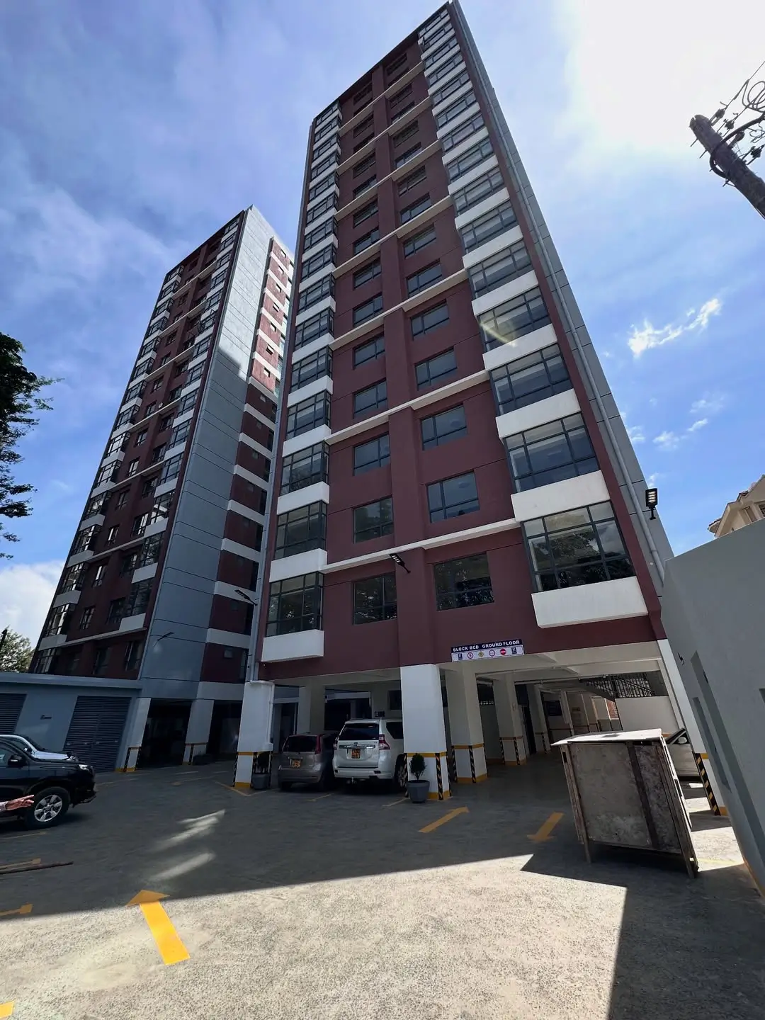 Multi-story residential building with red brick facade and ground level parking