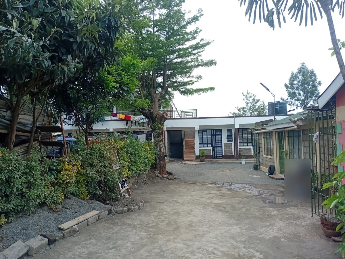 Compound entrance with mature trees and residential structures