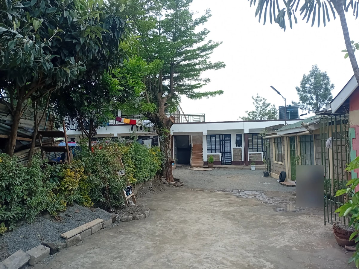 Compound entrance with mature trees and residential structures