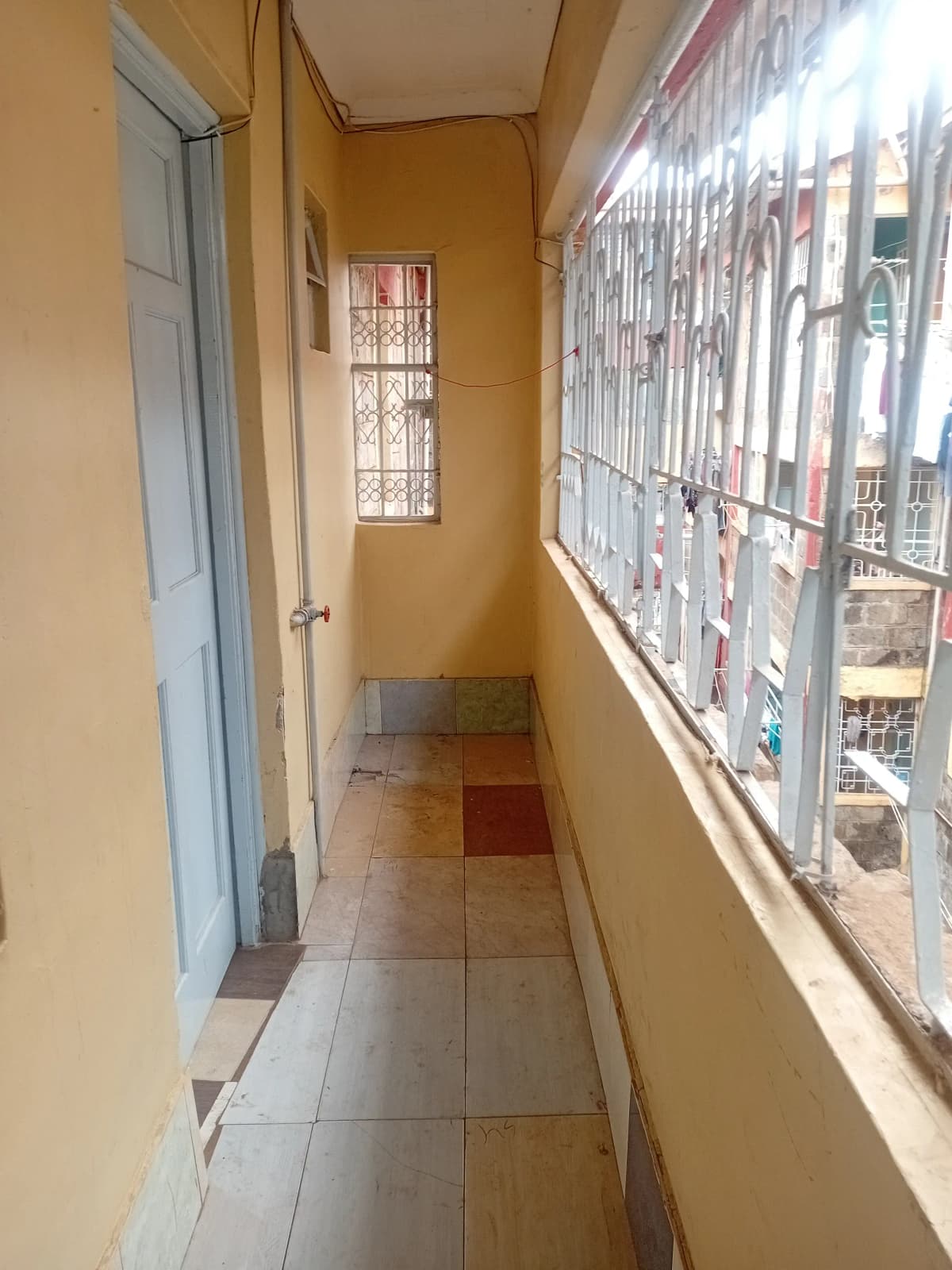 Narrow enclosed balcony with barred windows, city view.
