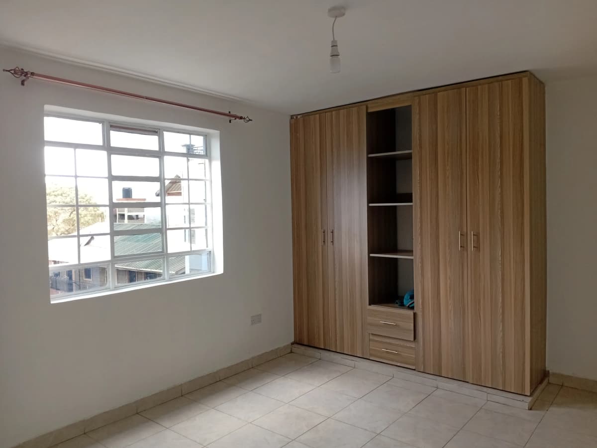 Bright bedroom with built-in wooden wardrobe and window view