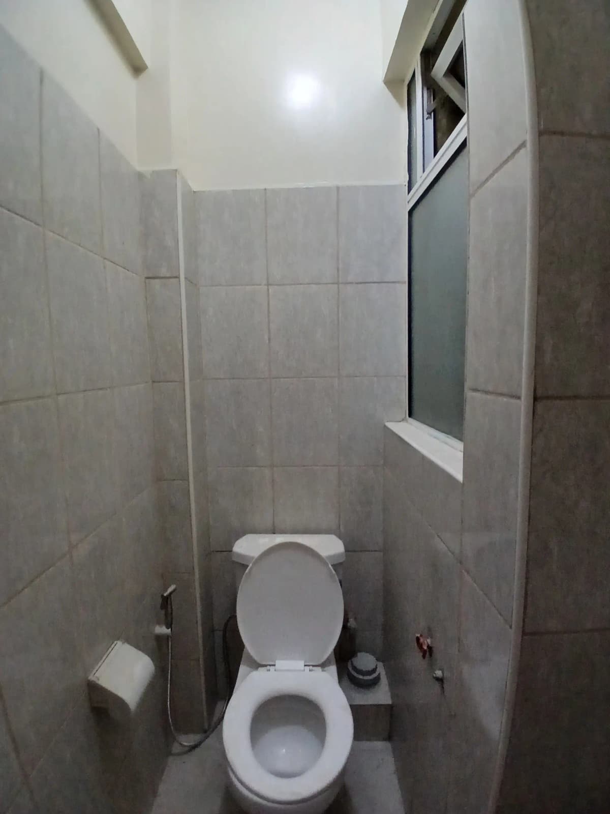 Compact toilet room with gray tiled walls and window